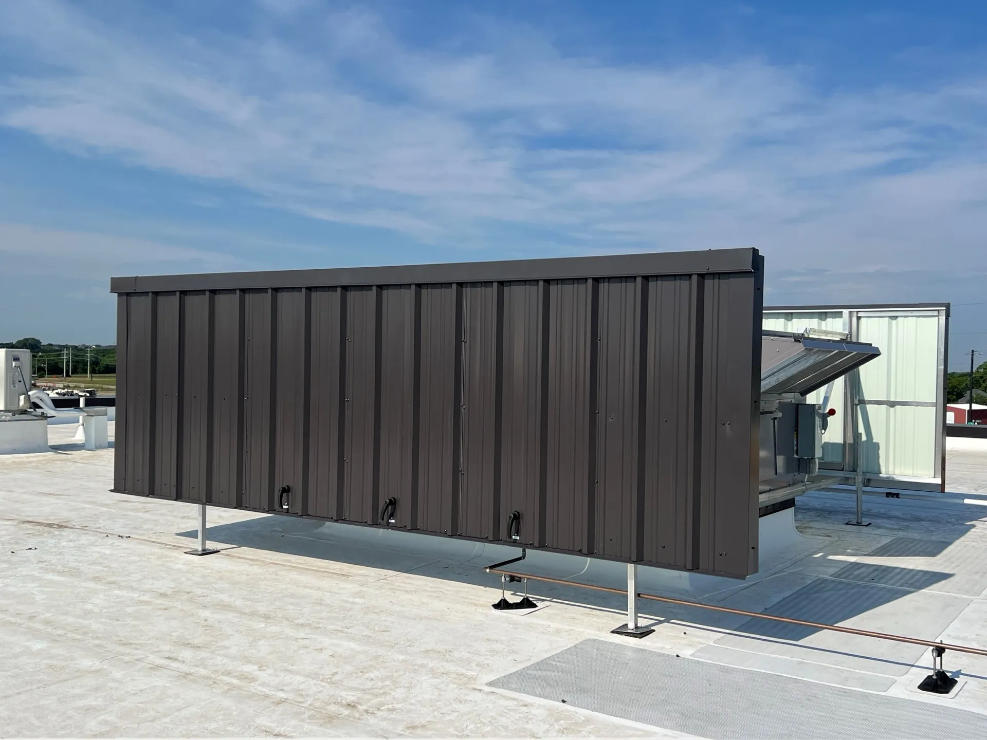 Dark corrugated steel RTU screen wall with access latches on a commercial roof